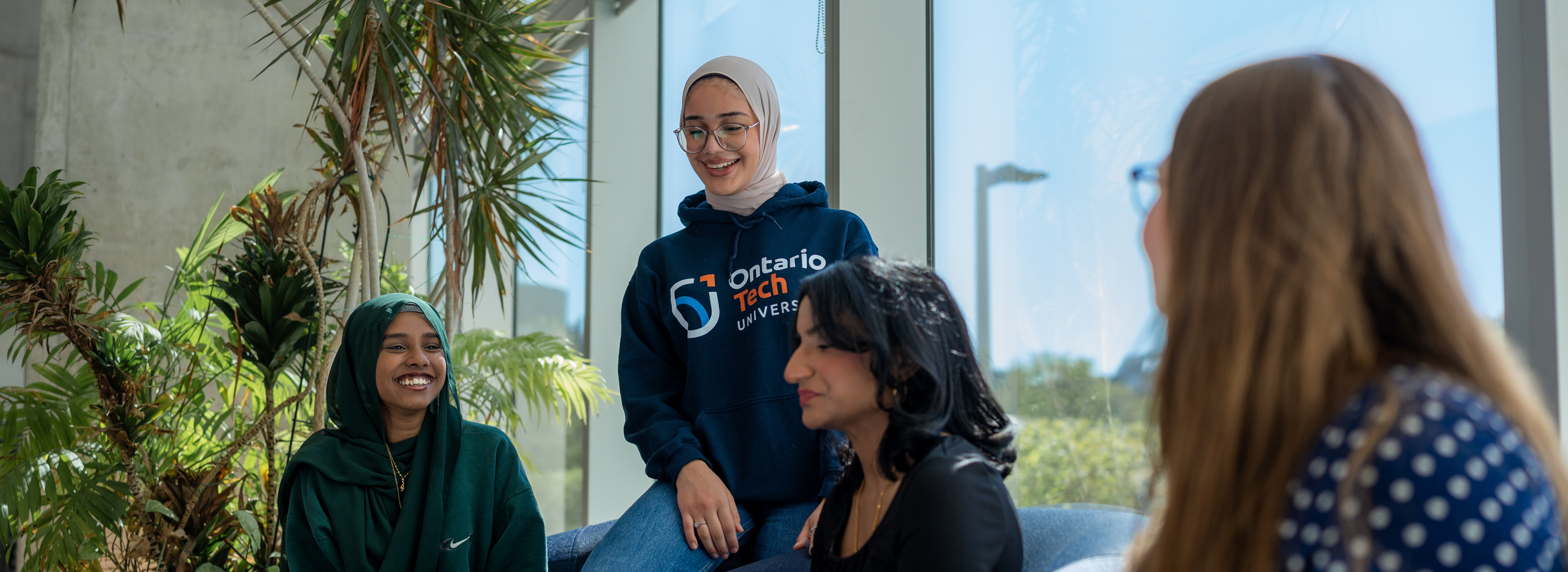 Four female students, seated and chatting together on a couch in a sunny room at the Student Learning Support services.